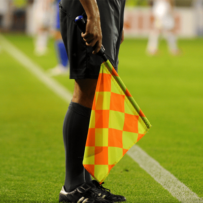 A curacao football referee member, standing on the football field with his flag.